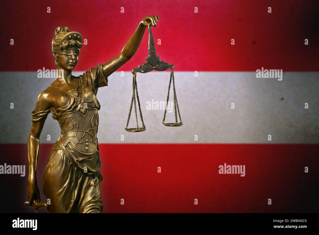 Close-up of a small bronze statuette of Lady Justice before an Austrian flag. Stock Photo