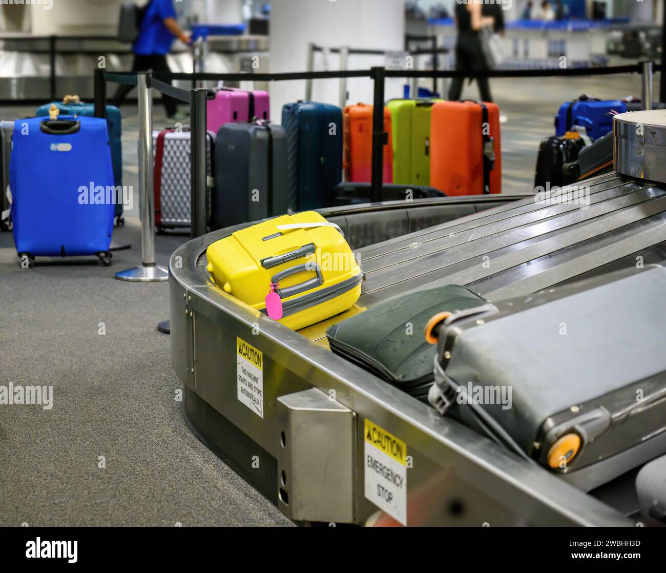 Suitcases on luggage conveyor belt in baggage claim at airport. Unclaimed luggages and unrecognisable people in the background. Stock Photo