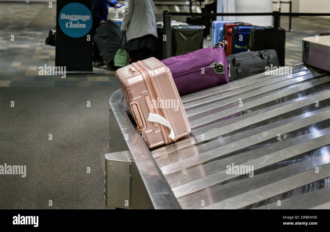 Suitcases on luggage conveyor belt in baggage claim at airport. Unrecognisable people collecting their luggages. Stock Photo