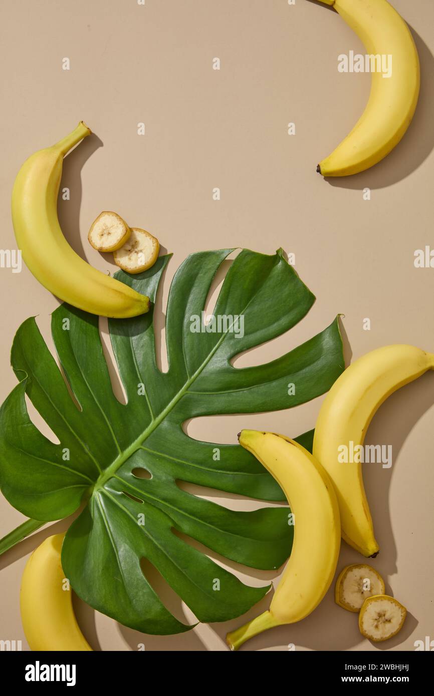 A tropical green leaf displayed with some bananas on beige background. Eating bananas regularly can improve nerve and brain function Stock Photo