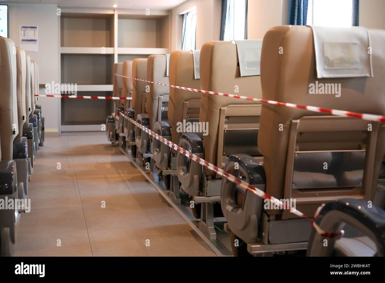 horizontal frame of a modern train car interior. The image showcases multiple rows of empty beige seats, sectioned off by red and white barrier tape i Stock Photo
