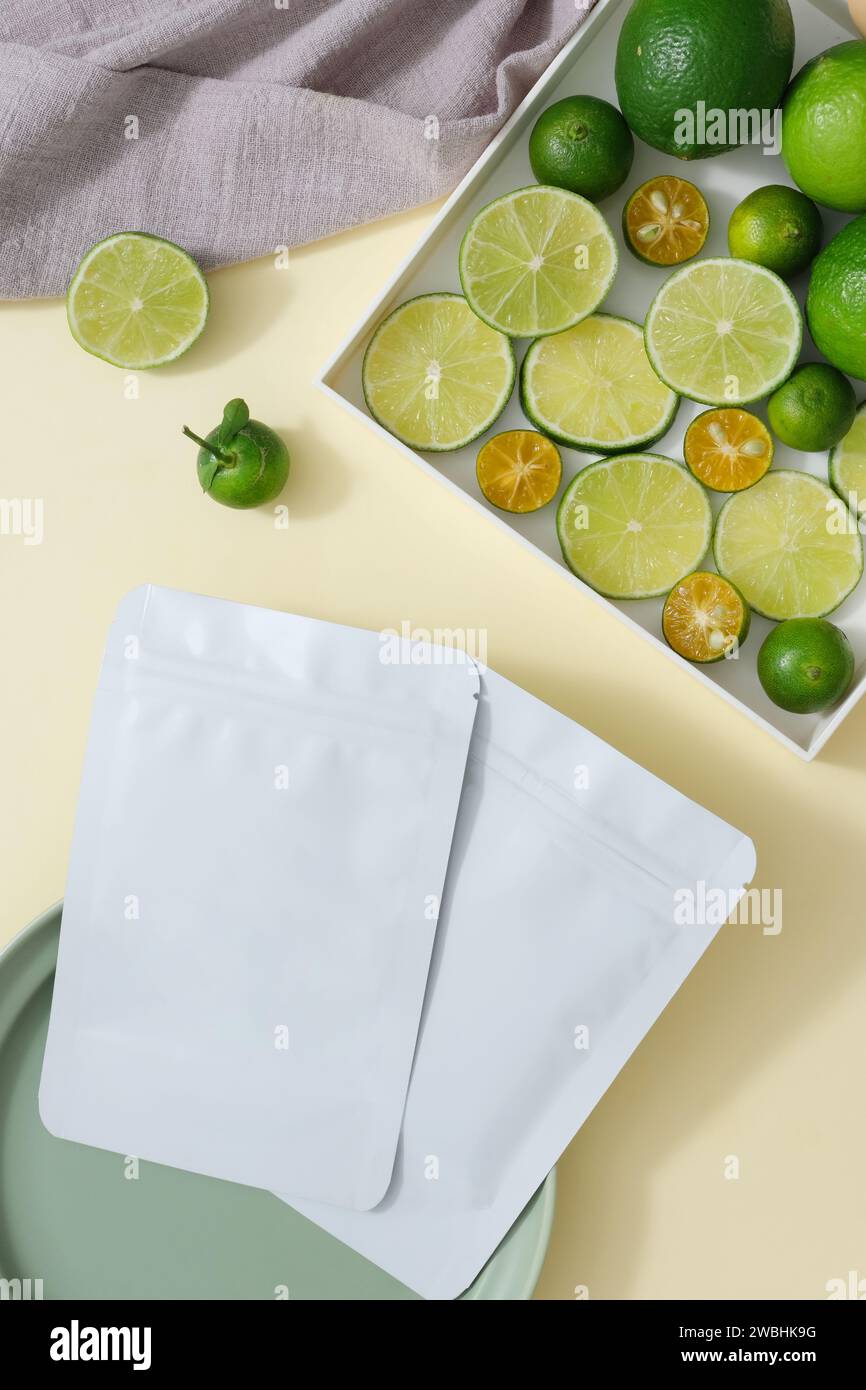 Facial mask sheet without label placed on a ceramic dish. A tray containing kumquat and lime slices displayed with a towel. Mockup template for brandi Stock Photo