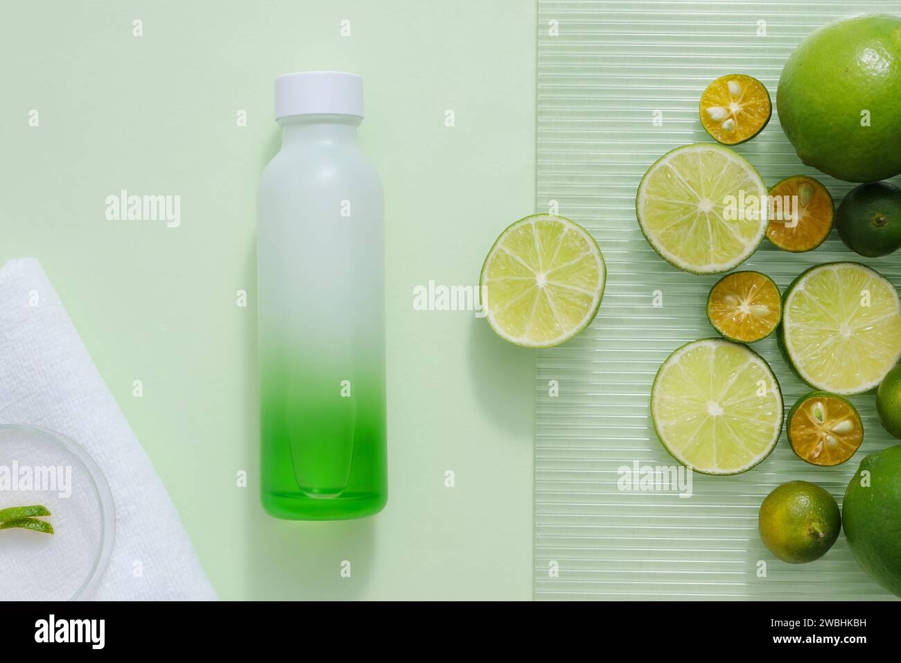 Unlabeled bottle in gradient green color displayed with many kumquat and lime round slices. White towel with a petri dish placed on. Template for bran Stock Photo
