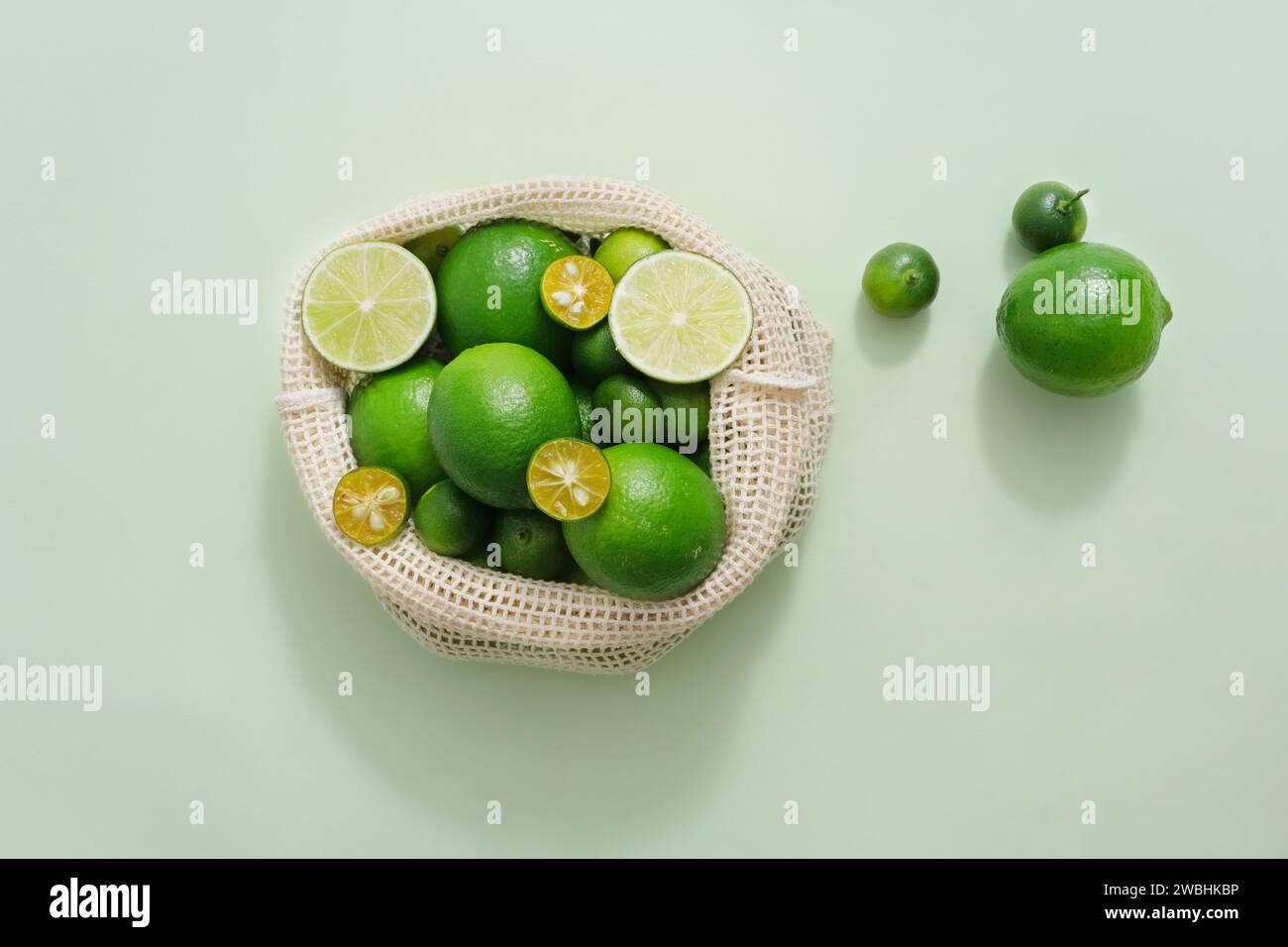 View from above of many kumquat and lime contained inside a mesh bag. Pastel background. Lime