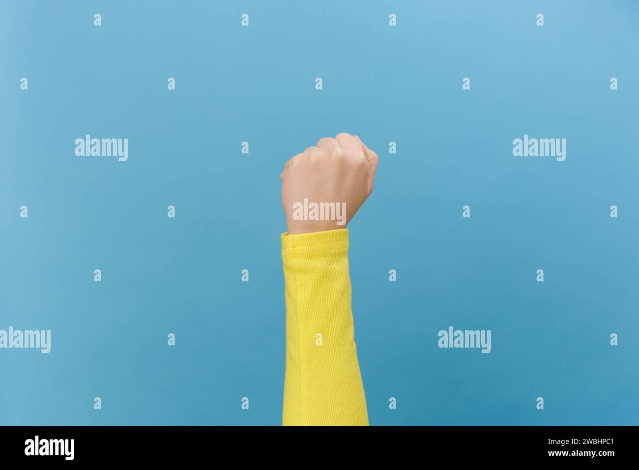 Close up of angry unrecognizable young woman shaking fist, isolated over blue studio background with copy space. Advertising area, mock up. Threat ges Stock Photo