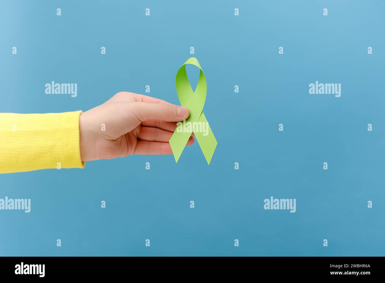 Close up of female hand holding green ribbon, posing isolated over blue ...