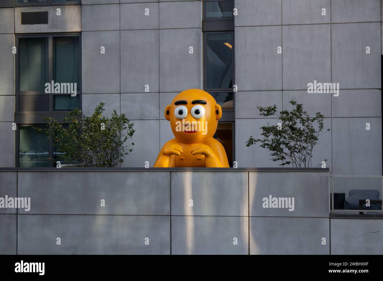 A vibrant yellow statue in front of a modern building in New York, United States Stock Photo