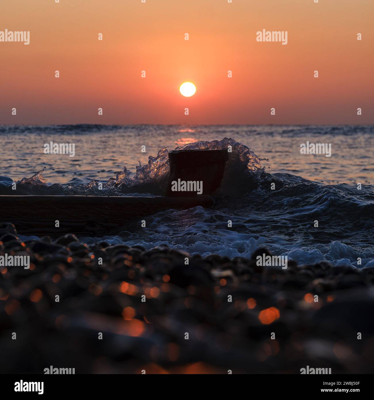 A bright orange sun rising behind a breaking wave sea on a Cold January ...
