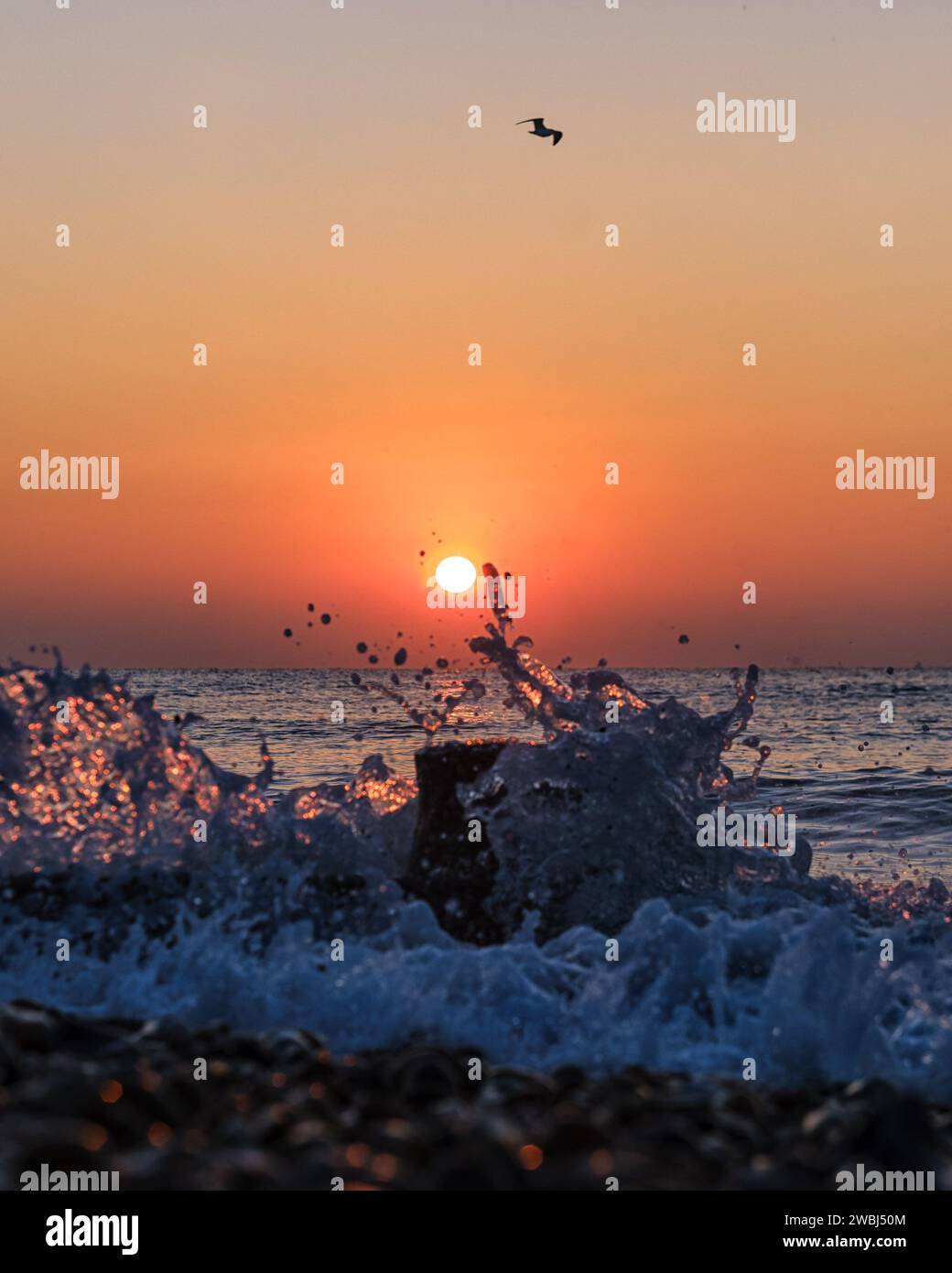 A bright orange sun rising behind a breaking wave sea on a Cold January ...