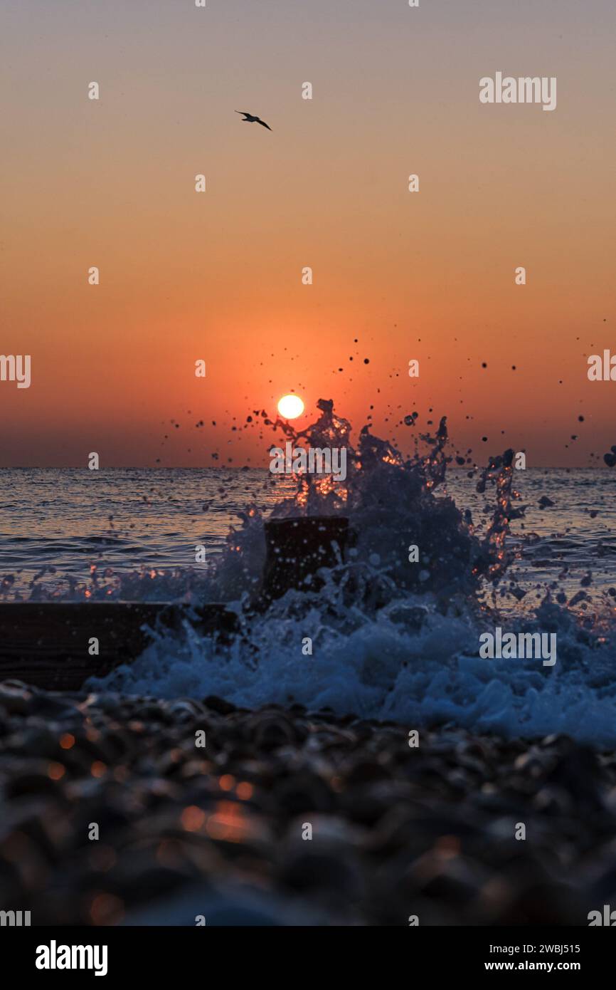 A bright orange sun rising behind a breaking wave sea on a Cold January ...