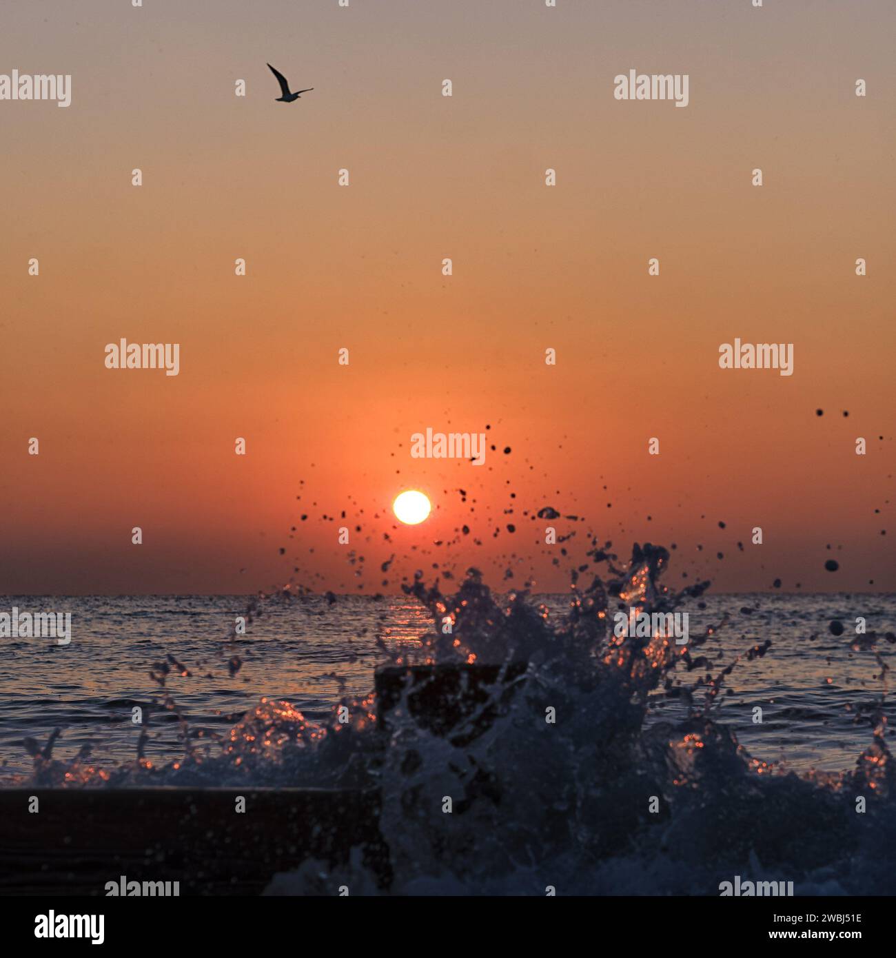 A bright orange sun rising behind a breaking wave sea on a Cold January ...