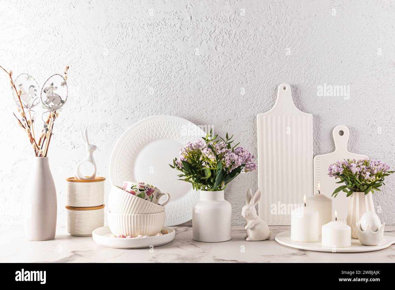 Chic kitchen background in delicate pastel colors, decorated for the Easter holiday with rabbits, candles, flowers, eggs. White cookware Stock Photo