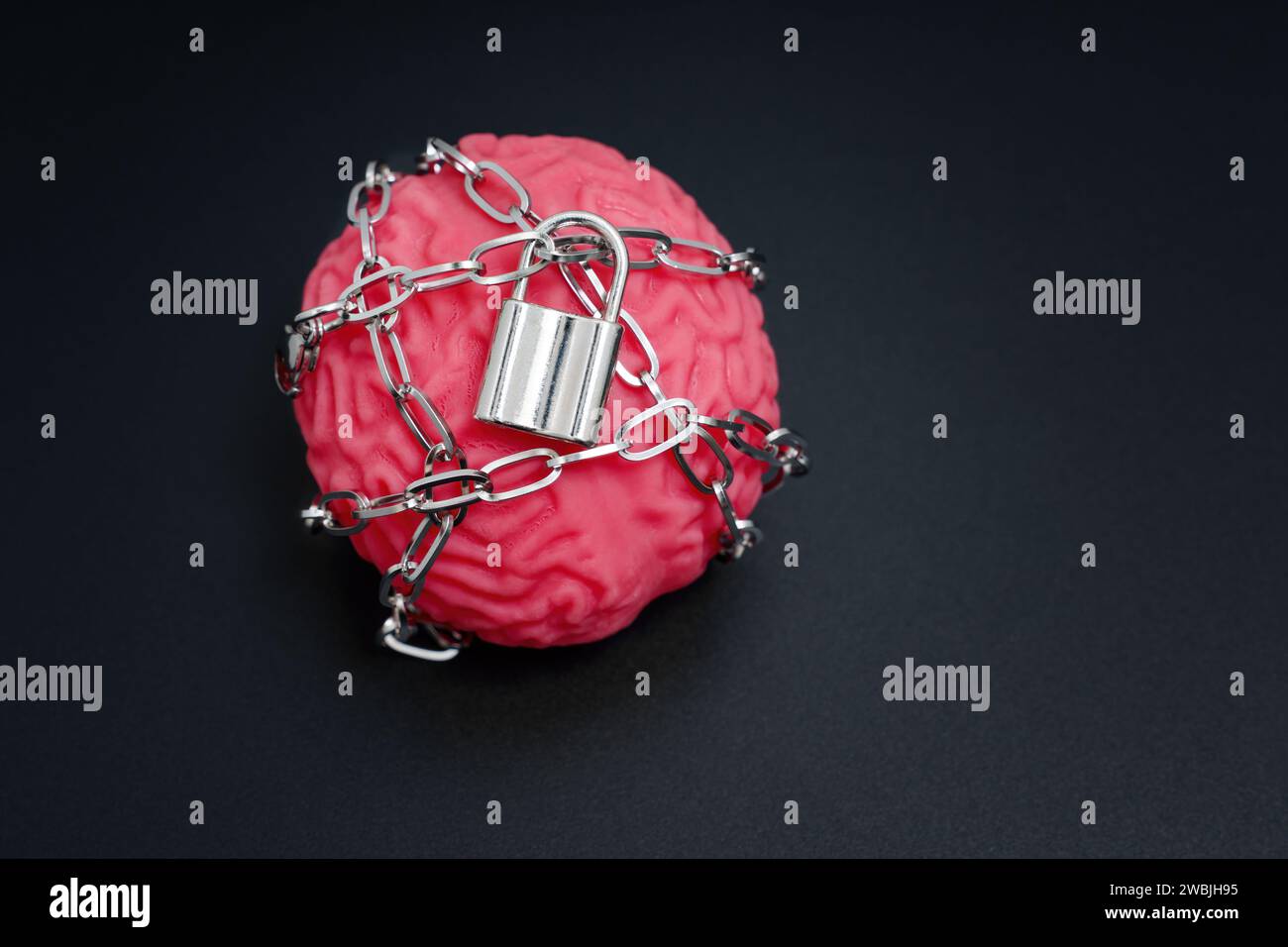 Close-up of a human brain model confined by chains and secured with a padlock isolated on black. Mental Imprisonment related concept. Stock Photo