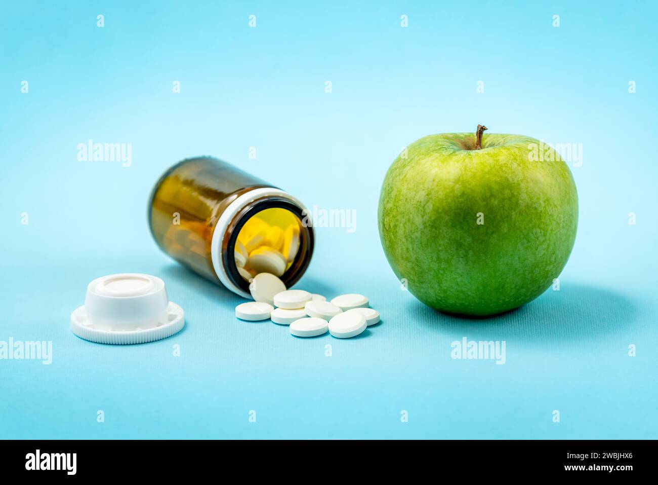 Green apple versus bottle of spilled pills medicaments isolated on