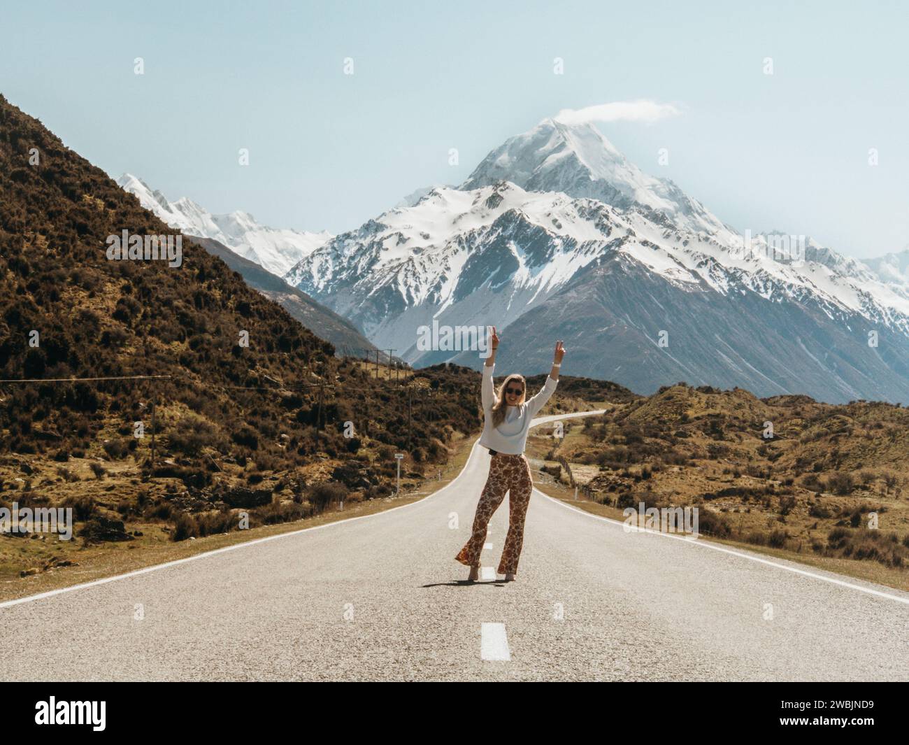Carefree girl walking on the road to Mt Cook, New Zealand wearing bohemian clothing. Stock Photo