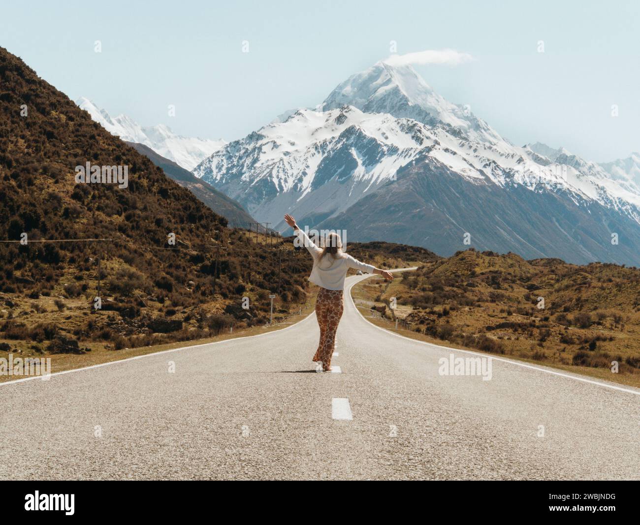 Carefree girl walking on the road to Mt Cook, New Zealand wearing bohemian clothing. Stock Photo