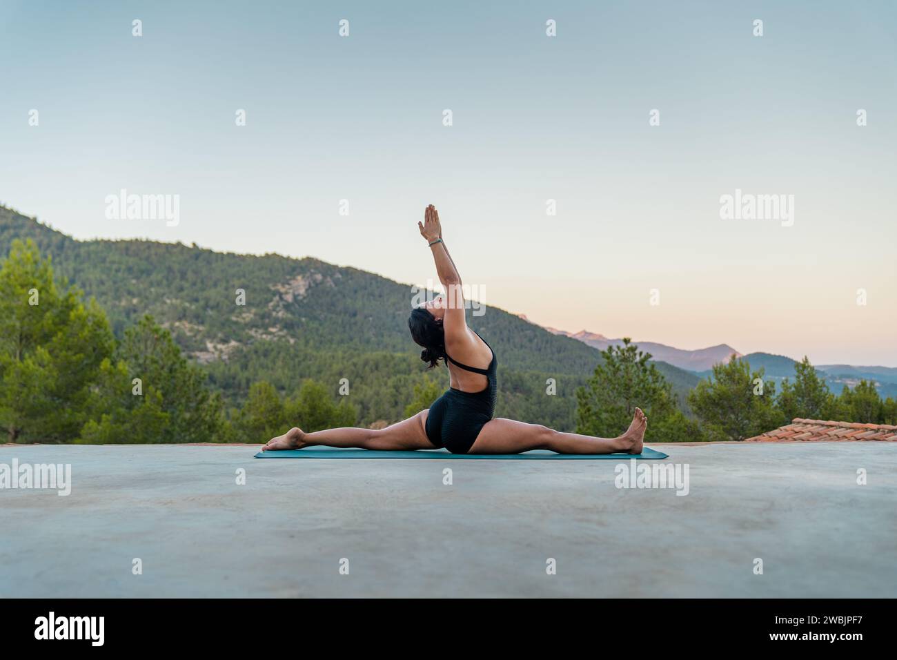 Young brunette girl practicing Hanumanasana or split pose with mountainous landscape in the background. Stock Photo