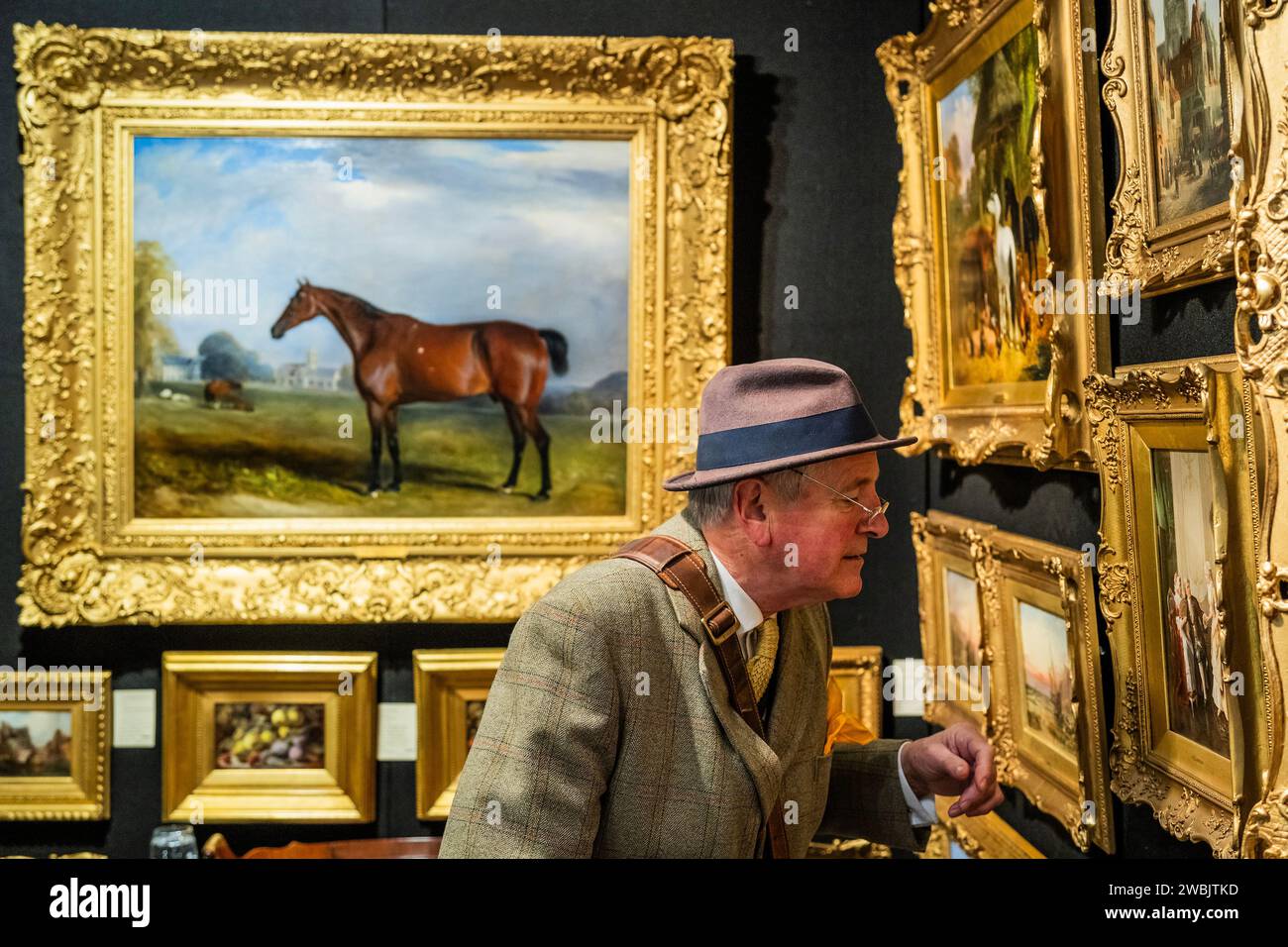 London, UK. 11th Jan, 2024. A collector examines oil paintings in