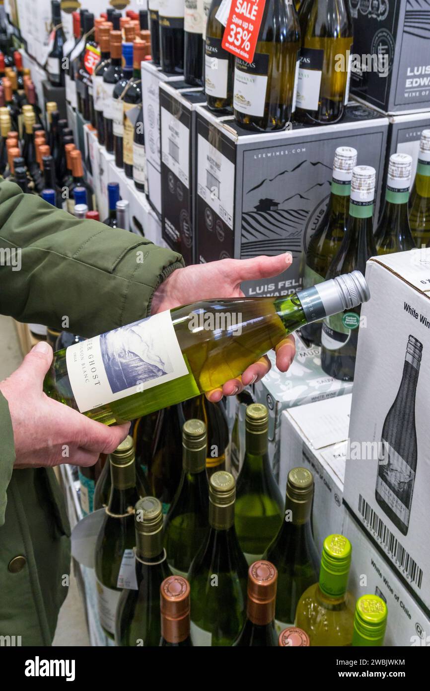 Woman reading the label of a bottle of Silver Ghost Chilean Sauvignon Blanc wine in a Majestic Wine off-licence. Stock Photo
