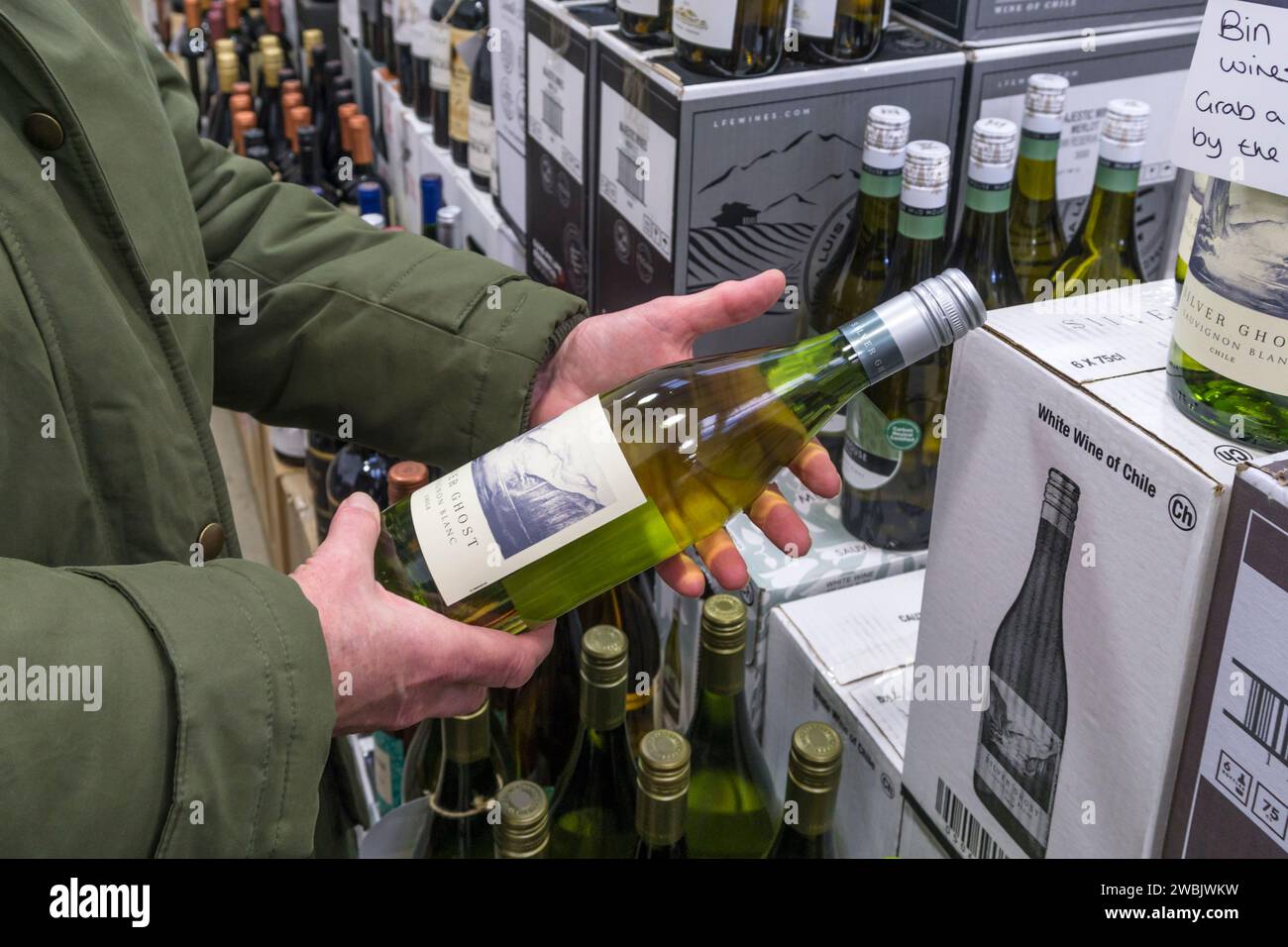 Woman reading the label of a bottle of Silver Ghost Chilean Sauvignon Blanc wine in a Majestic Wine off-licence. Stock Photo
