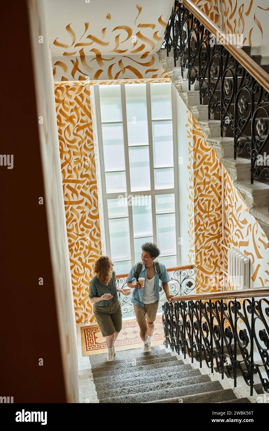 interracial couple with smartphone and paper cup walking on staircase ...