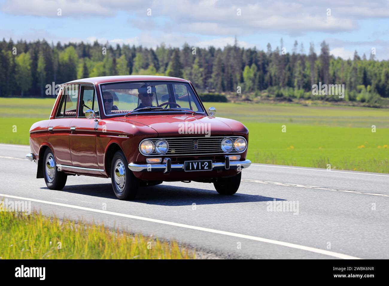Beautiful red Datsun 1300 classic car year 1967 moving along highway on a sunny day of summer. Jokioinen, Finland. June 9, 2023. Stock Photo