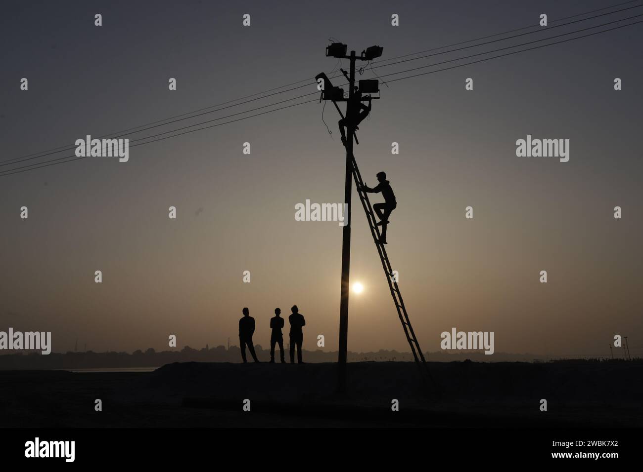 Prayagraj, India. 11 January 2024, Indian labourers fix electric cables and flood lights  at the banak of river Ganges during the prepraion for the upcoming one month long Magh Mela 2024 , in Prayagraj, India.  Credit: Anil Shakya/Alamy Live News Stock Photo