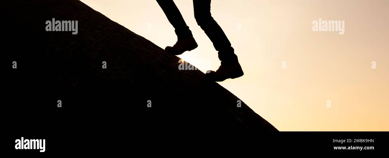 Legs with mountain boots on a mountain peak against the light Stock Photo
