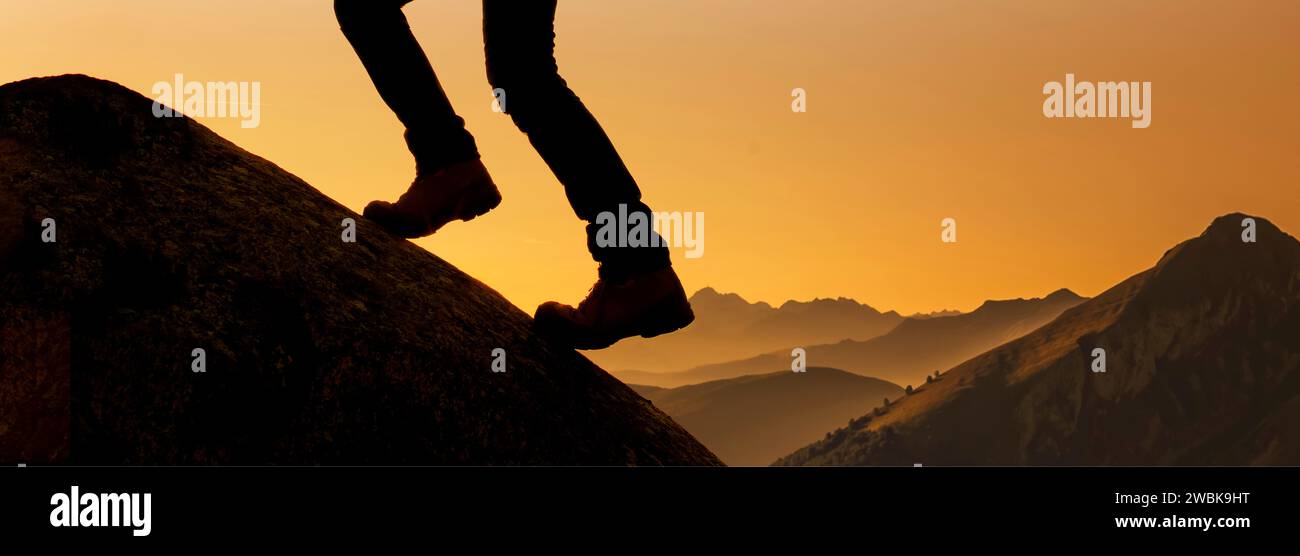 Legs with mountain boots on a mountain peak against the light Stock Photo