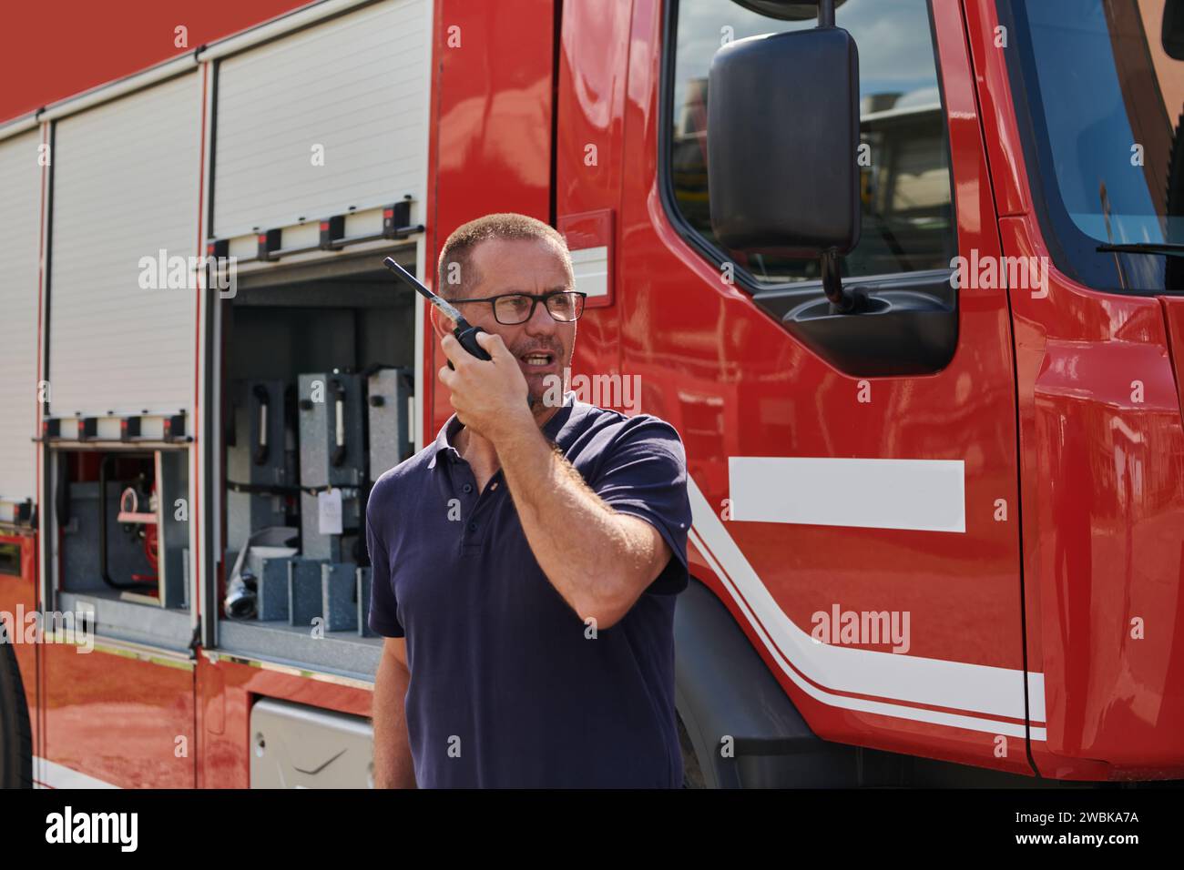 A dedicated firefighter, captured in a moment of communication, stands before a modern firetruck, showcasing the seamless integration of technology in Stock Photo