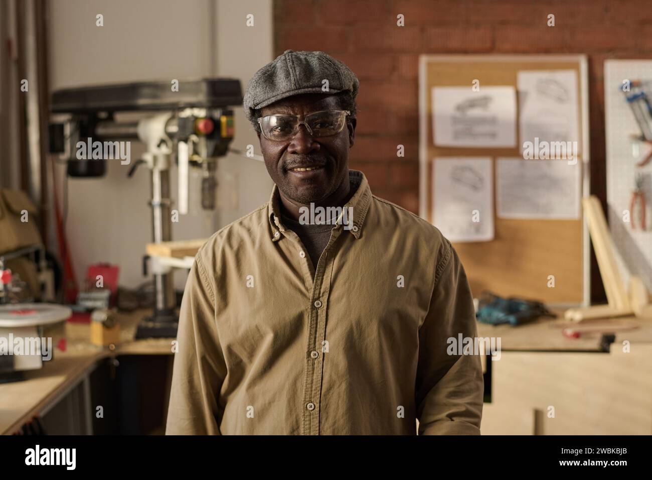 Portrait of kind Black senior craftsman wearing protective glasses and smiling at camera in workshop Stock Photo