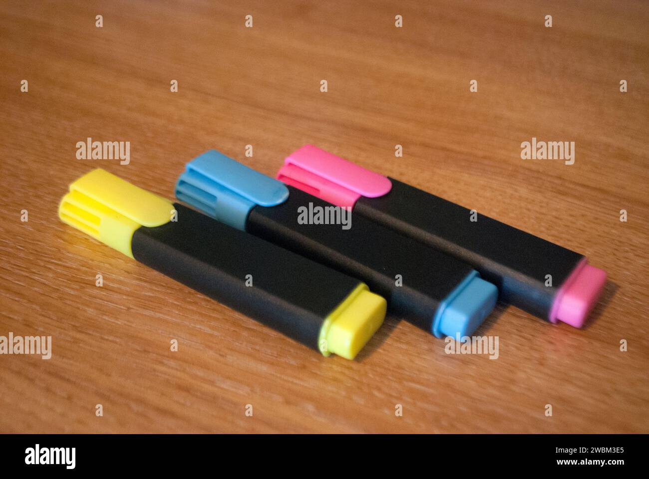 Three highlighter pens with yellow, cyan and magenta color tops on a desk Stock Photo