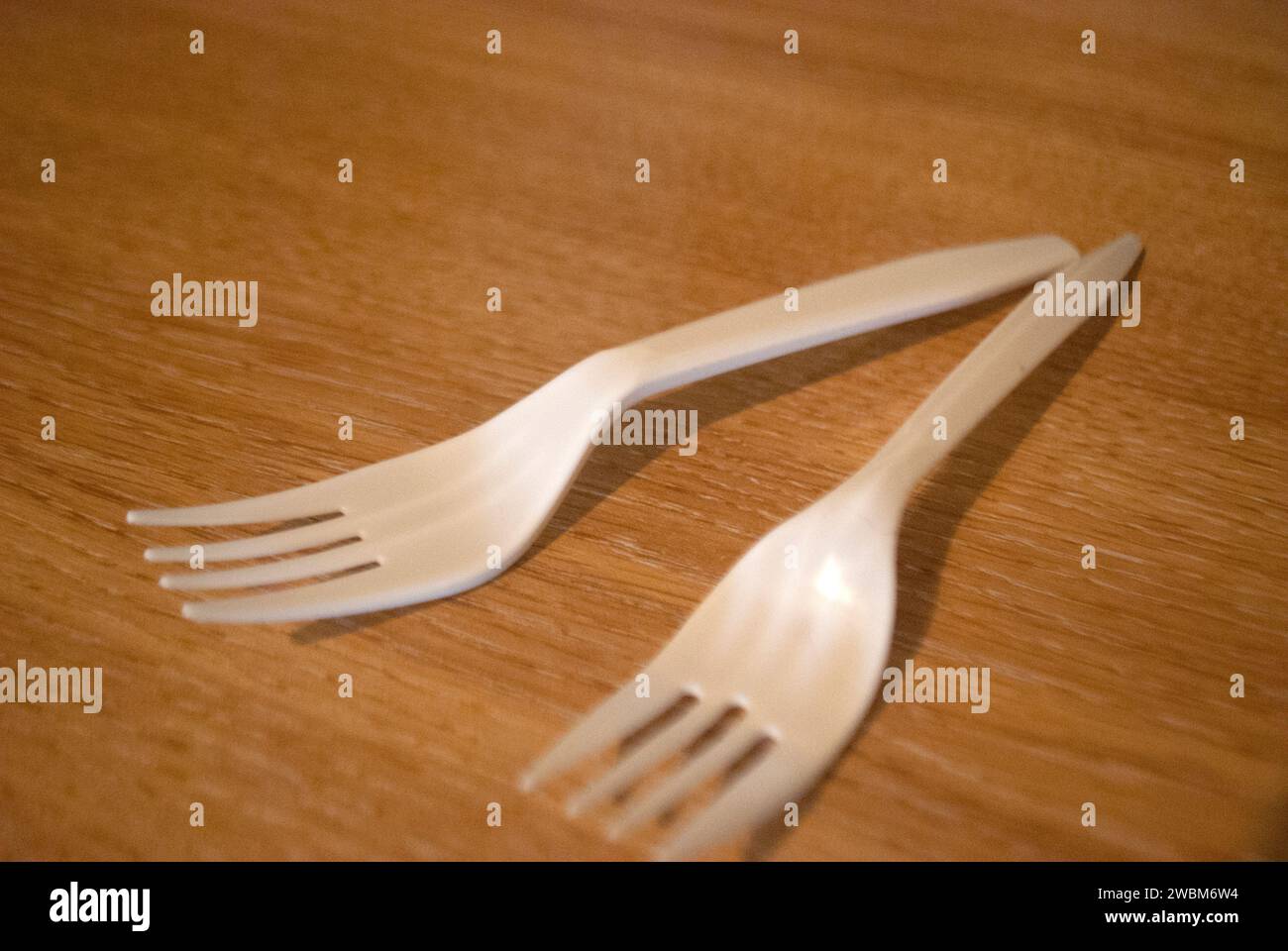Two white plastic forks on a wood grain surface Stock Photo