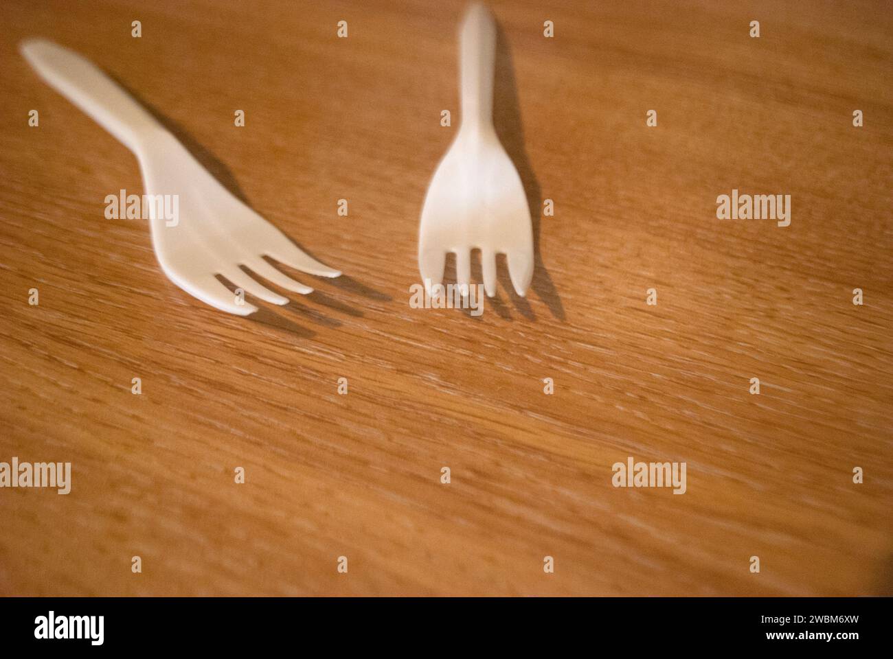 Two white plastic forks on a wood grain surface Stock Photo
