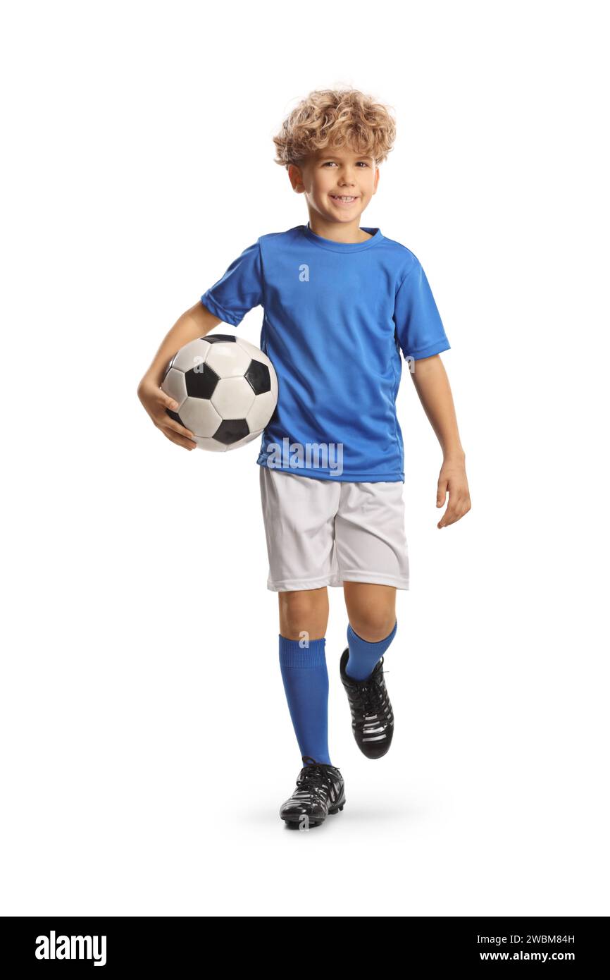 Full length portrait of a boy in a football kit walking and carrying a ball isolated on white background Stock Photo
