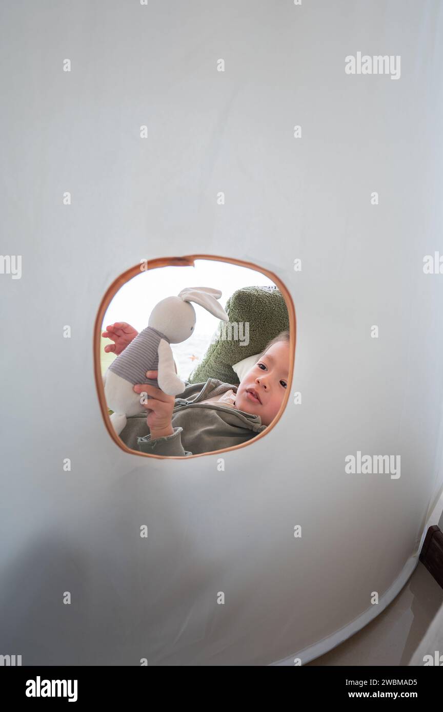 Adorable two and a half little boy is playing with soft toy rabbit in a white kids tent. Boy having fun as he sails through a fantasy world with his s Stock Photo