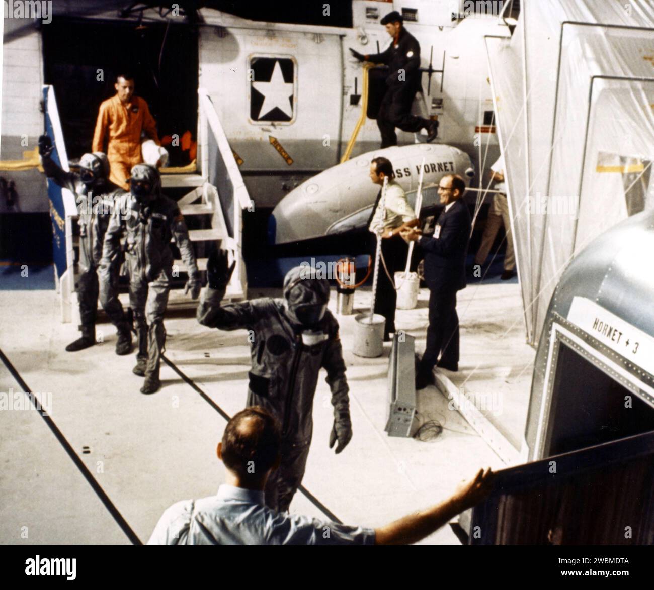 JOHNSON SPACE CENTER, HOUSTON, TEXAS - A technician aboard the USS Hornet holds the Mobile Quarantine Facility door open for the Apollo 11 astronauts as they leave the recovery helicopter. Astronauts, left to right, Edwin E. Aldrin Jr., Neil A. Armstrong and Michael Collins were taken to the USS Hornet after their Lunar Landing mission came to a successful completion at 12 50 p.m. EDT. Stock Photo