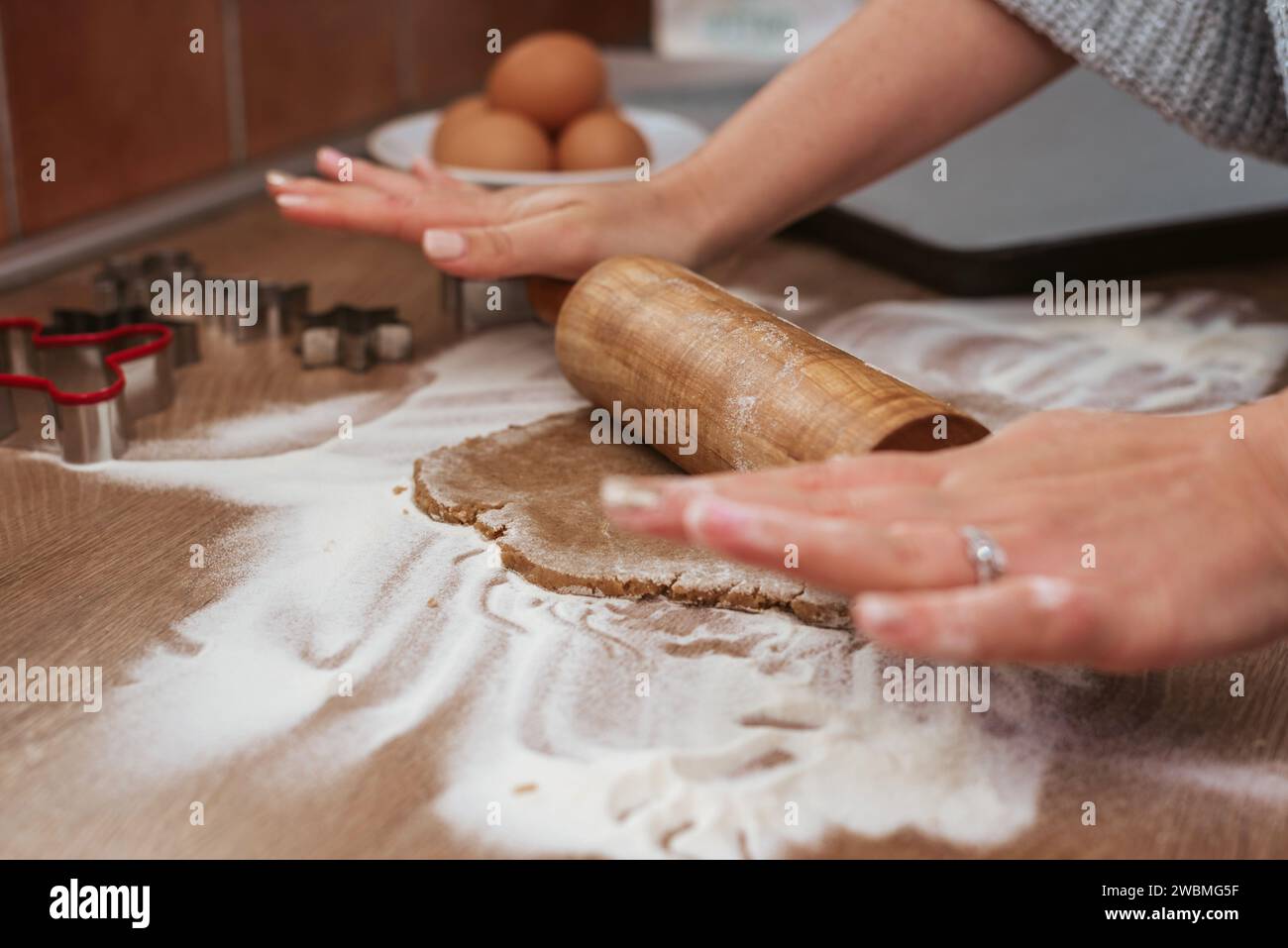 A female baker is carefully preparing dough for a recipe using a wooden spoon and two eggs on a kitchen countertop Stock Photo