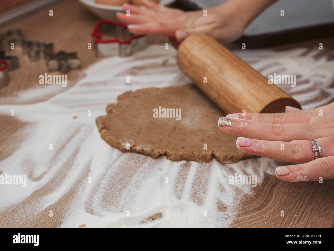 A Caucasian female chef stands in her kitchen, rolling out dough on a wooden countertop Stock Photo
