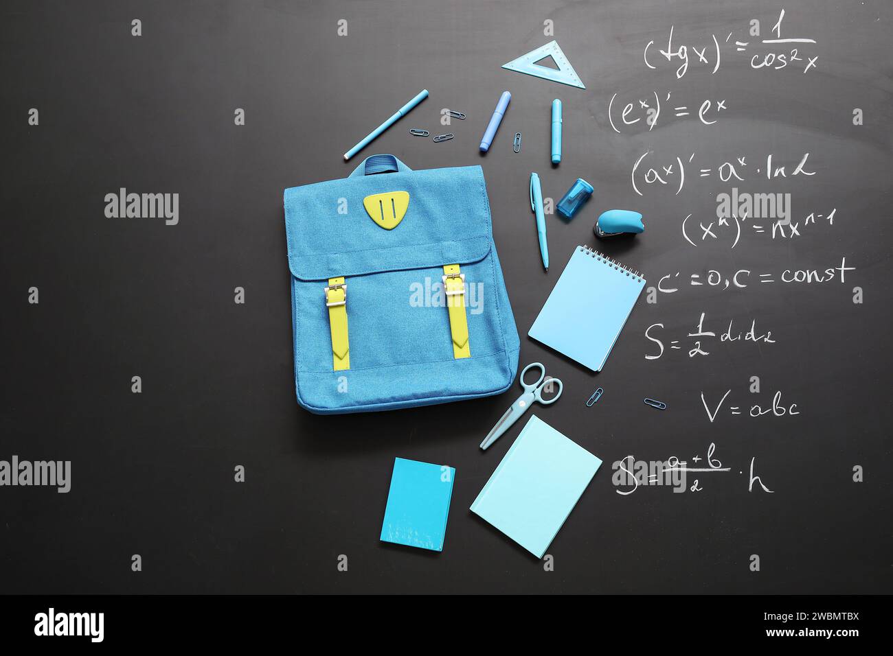 Blue school backpack with different stationery on black chalkboard painted with formulas Stock Photo
