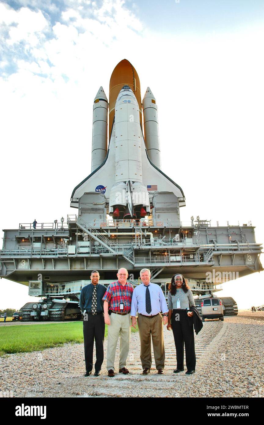 KENNEDY SPACE CENTER, FLA. - Space Shuttle Discovery, on top of the Mobile Launcher Platform and Crawler-Transporter, makes its way along the crawlerway to Launch Pad 39B. Getting a close look at the operation is Center Director Jim Kennedy (second from right), flanked by (on the left) Prentice Washington, intern for Deputy Director Woodrow Whitlow Jr., and Associate Director Jim Hattaway, and (on the right) Hortense Burt, intern for Kennedy. This is the second rollout of Discovery after being returned to the Vehicle Assembly Building for connection to an improved External Tank. Launch of Disc Stock Photo