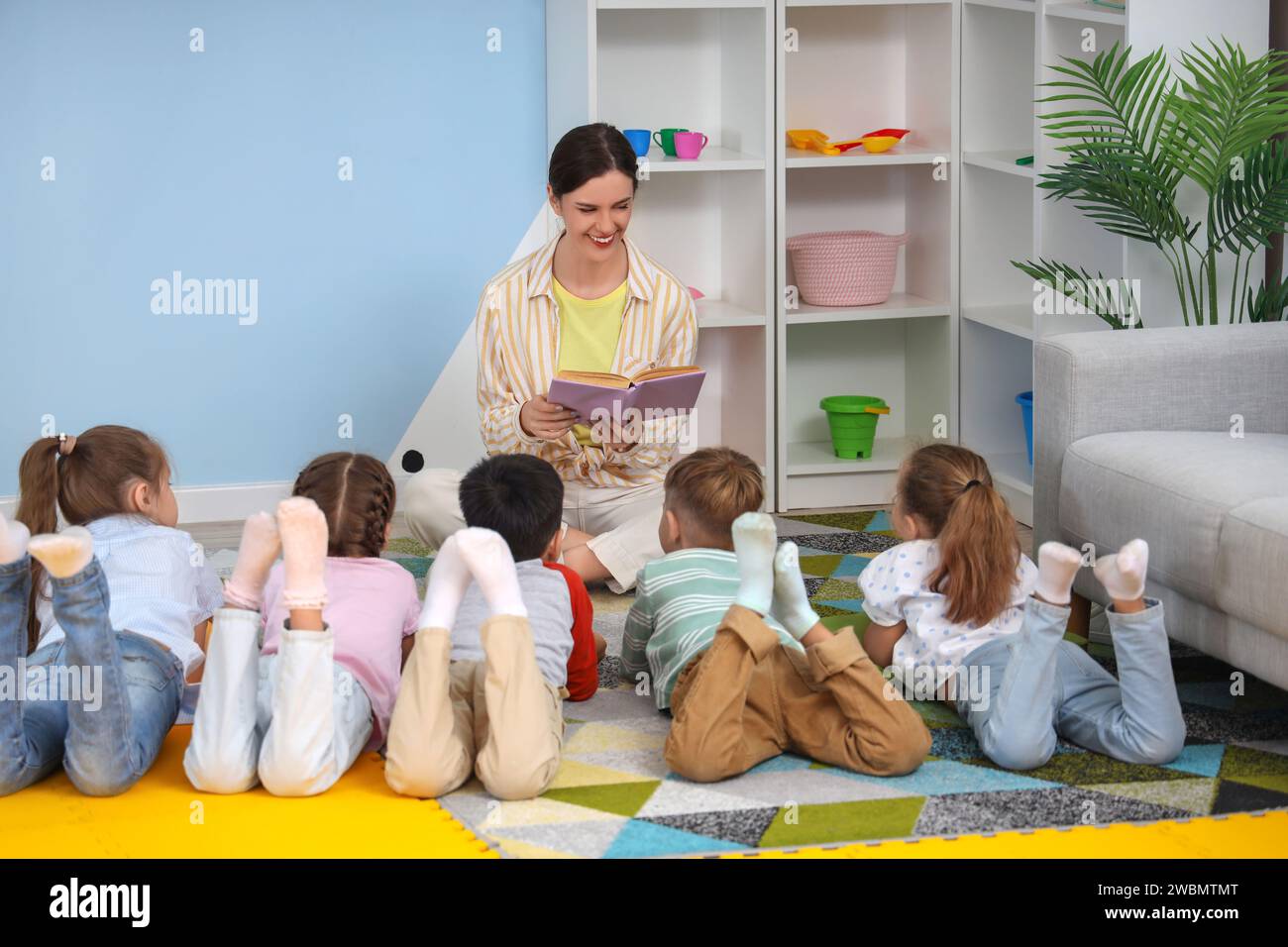 Nursery teacher reading story to little children in kindergarten Stock Photo