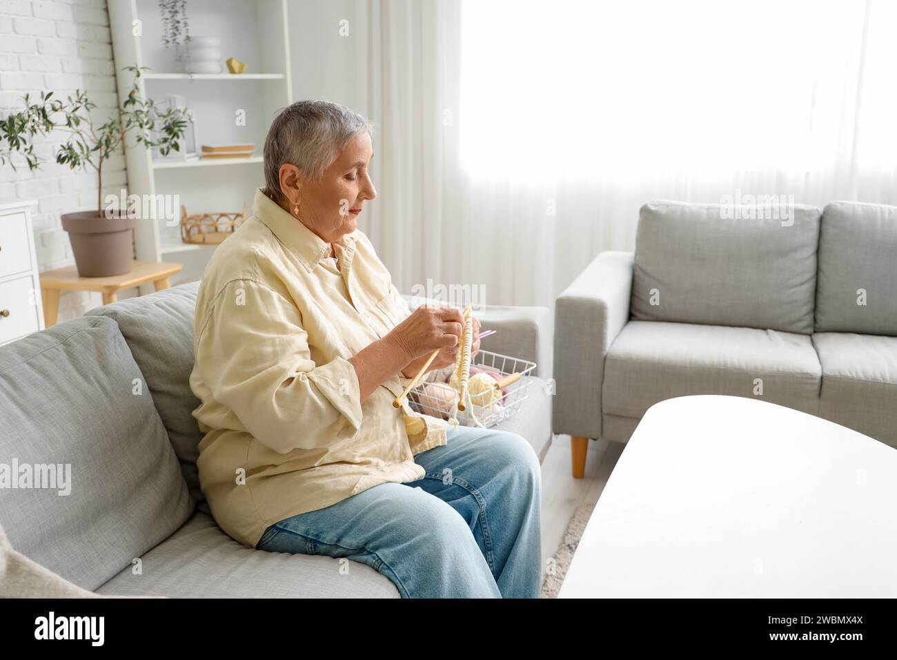 Senior woman knitting on sofa at home Stock Photo - Alamy