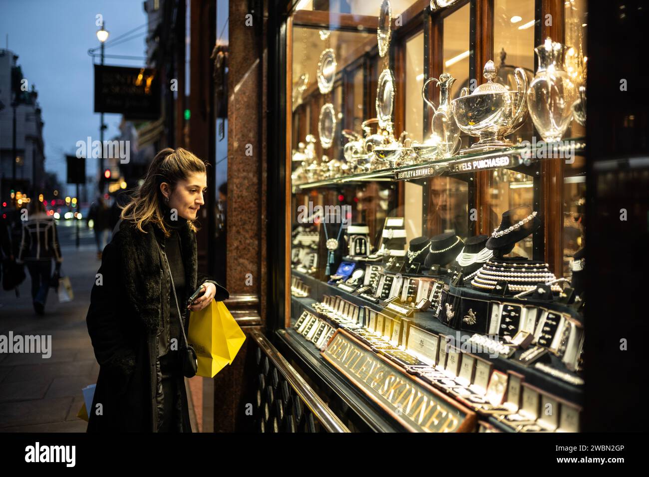 A young woman looks at some of the expensive jewellery and silverware on display at Bentley & Skinner, situated on Piccadilly, in the heart of Mayfair. Stock Photo