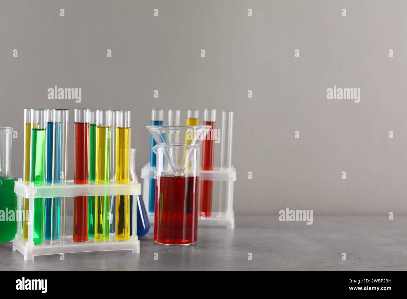 Test tubes with liquids in stand and flasks on table against light grey ...
