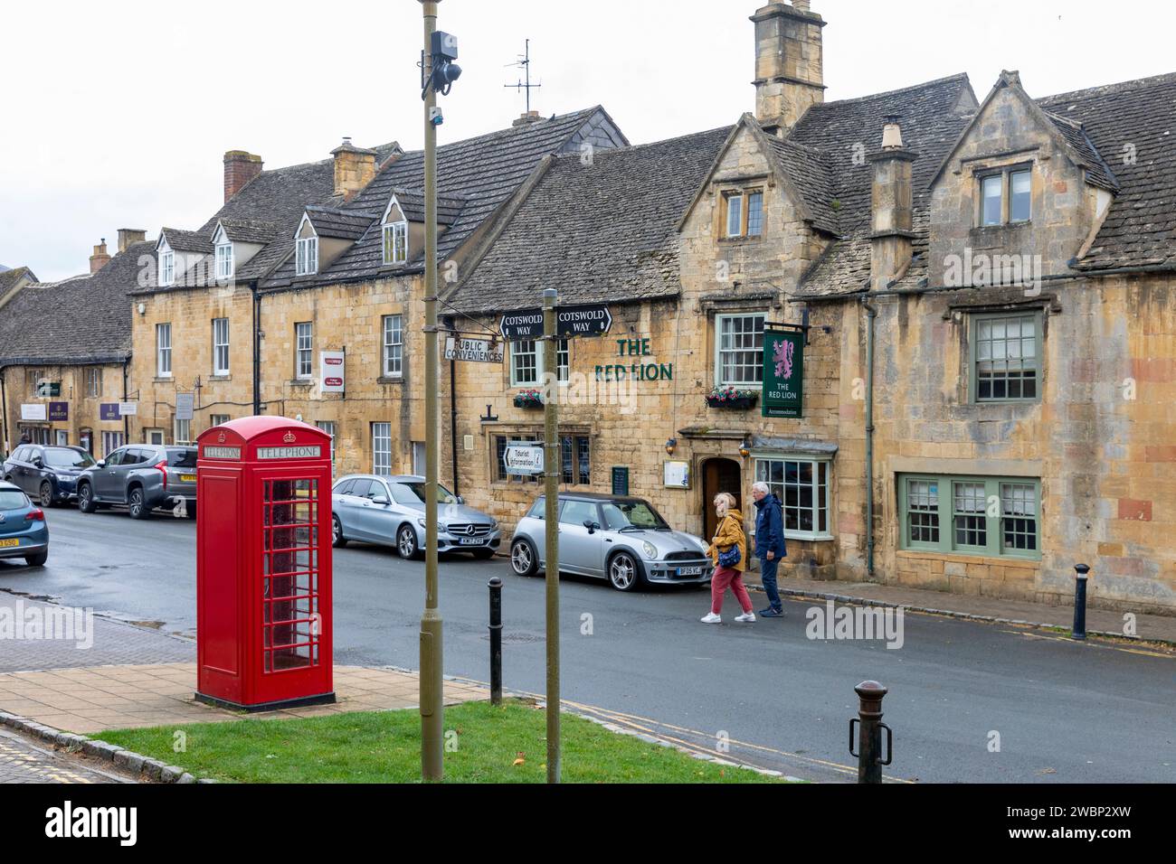 The Red Lion pub in Chipping Campden high street, traditional red London phone box, couple cross the road,England,UK,2023 Stock Photo