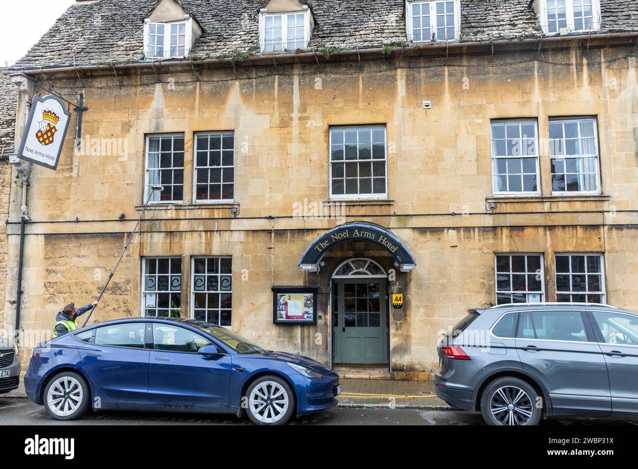 Chipping Campden ancient market town, Noel Arms Hotel in lower high street, man cleaning windows, pub and hotel,England,UK,2023 Stock Photo