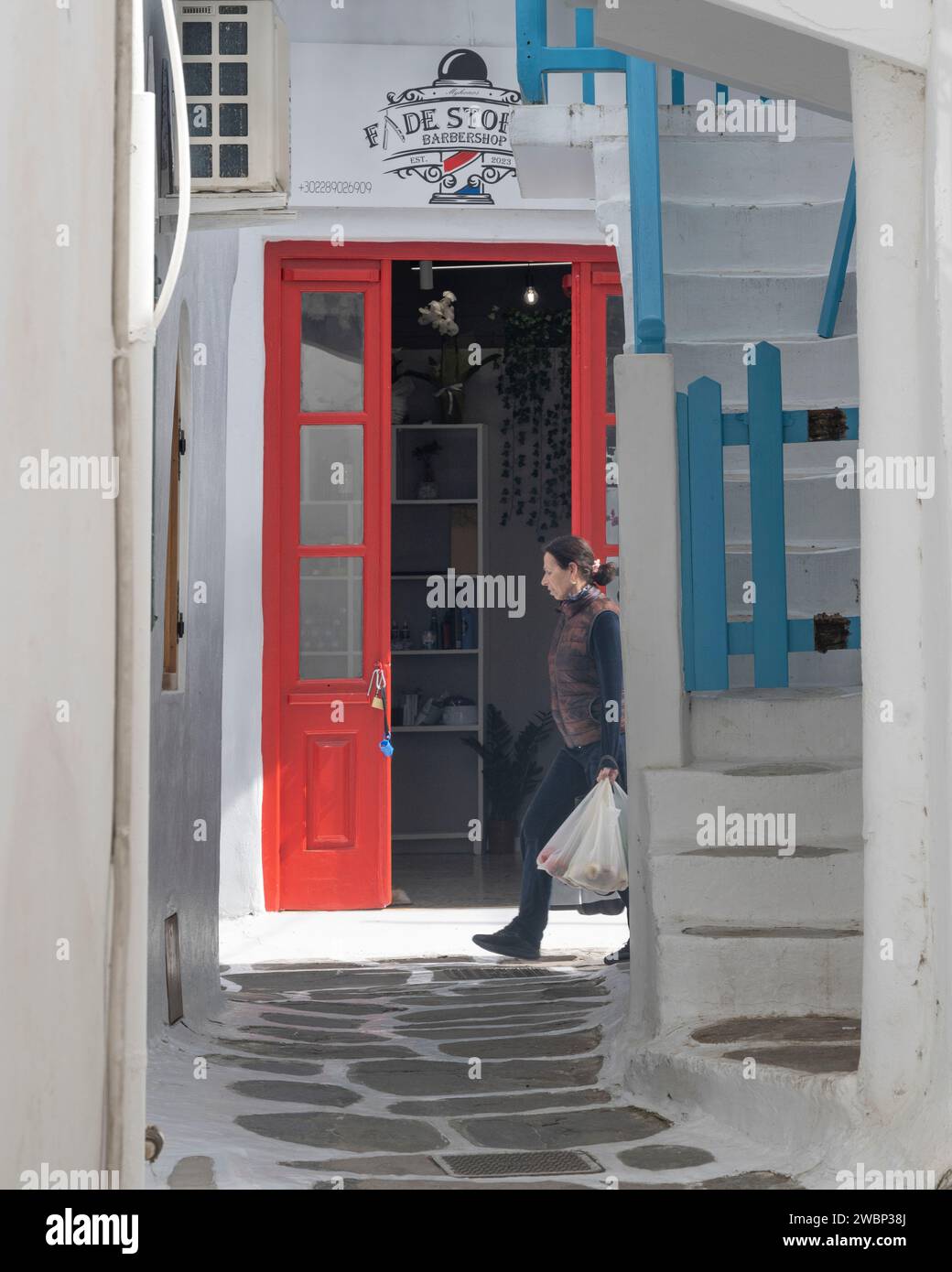 Woman holding a shopping bag, walking along a narrow alley in Mykonos Town, Mykonos Island, South Aegean, Greece Stock Photo