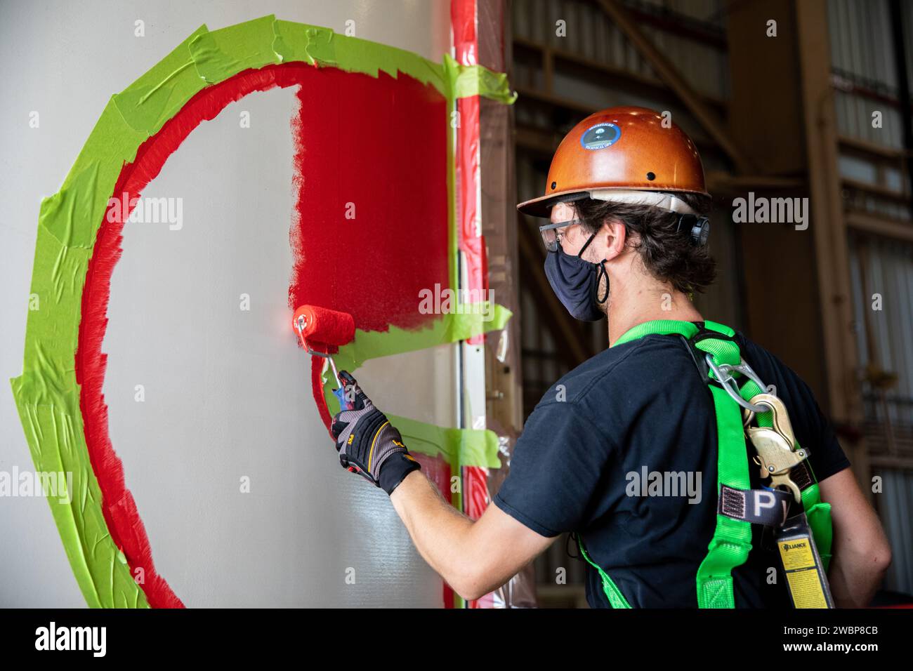 A worker with NASA’s Exploration Ground Systems (EGS) finishes the first coat of the bright red “worm” logo taking shape on the side of an Artemis I solid rocket booster segment inside the Rotation, Processing and Surge Facility (RPSF) at Kennedy Space Center in Florida. The EGS team used a laser projector to mask off the logo with tape, then painted the first coat of the iconic design. The booster segments will help propel the Space Launch System (SLS) rocket on Artemis I, a test of the Orion spacecraft and SLS as an integrated system ahead of crewed flights to the Moon. Northrop Grumman, whi Stock Photo