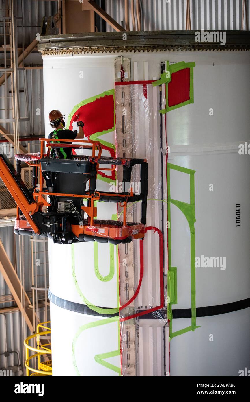 A worker with NASA’s Exploration Ground Systems (EGS) applies bright red paint to the agency’s “worm” logo taking shape on the side of an Artemis I solid rocket booster segment inside the Rotation, Processing and Surge Facility (RPSF) at Kennedy Space Center in Florida. The EGS team used a laser projector to mask off the logo with tape, then painted the first coat of the iconic design. The booster segments will help propel the Space Launch System (SLS) rocket on Artemis I, a test of the Orion spacecraft and SLS as an integrated system ahead of crewed flights to the Moon. Northrop Grumman, whic Stock Photo